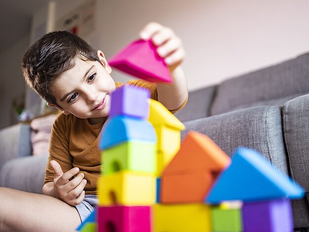 Kleiner Junge sitzt auf dem Wohnzimmerboden und spielt mit bunten Holzklötzen